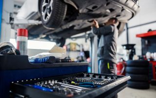 A mechanic working under a lifted car with a toolset in the foreground.