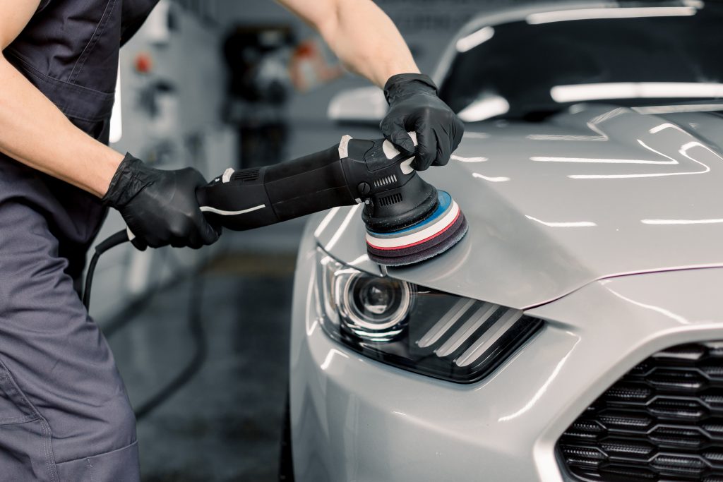 Car detailing and polishing concept. Hands of professional car service male worker, with orbital polisher, polishing white luxury car hood in auto repair shop Burlington Oil Change Services